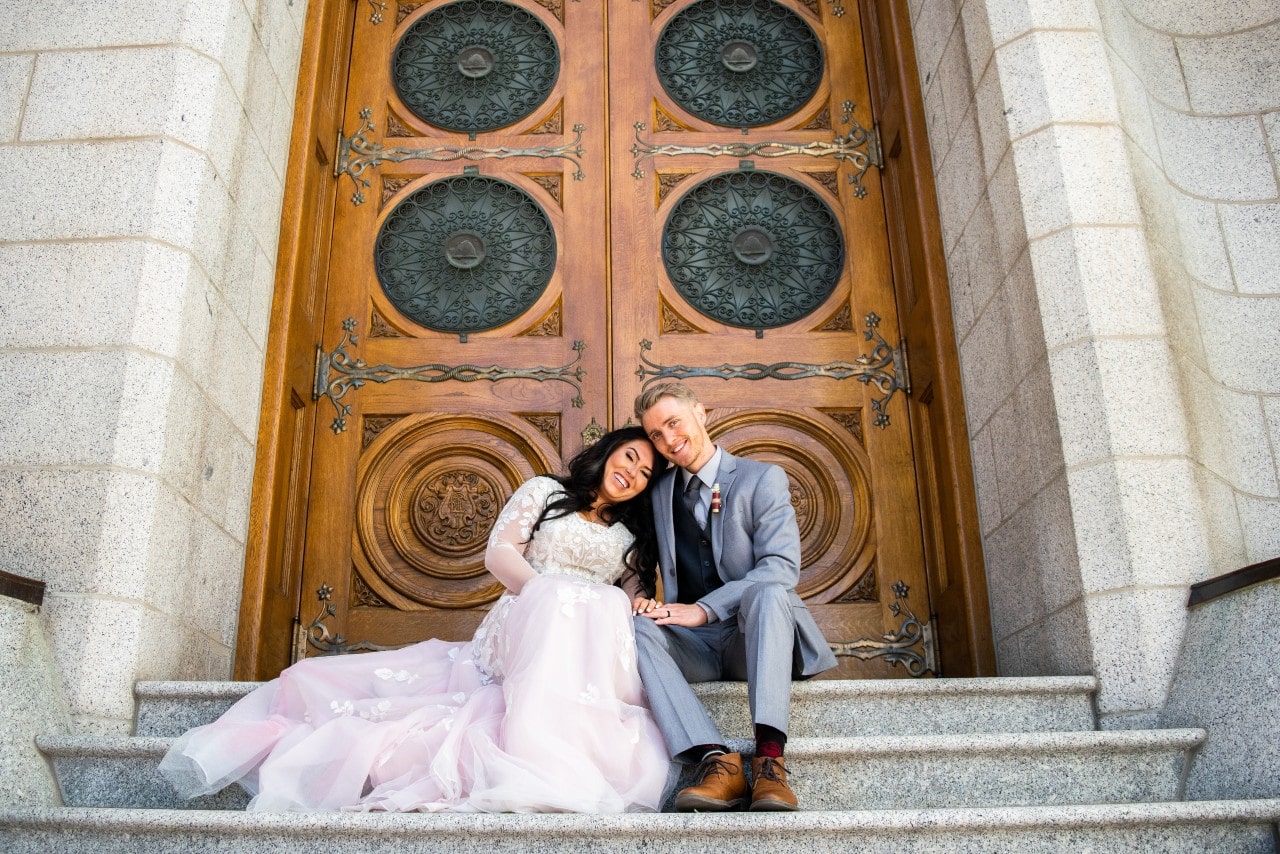 a bride and groom sitting on concrete steps outside a church building