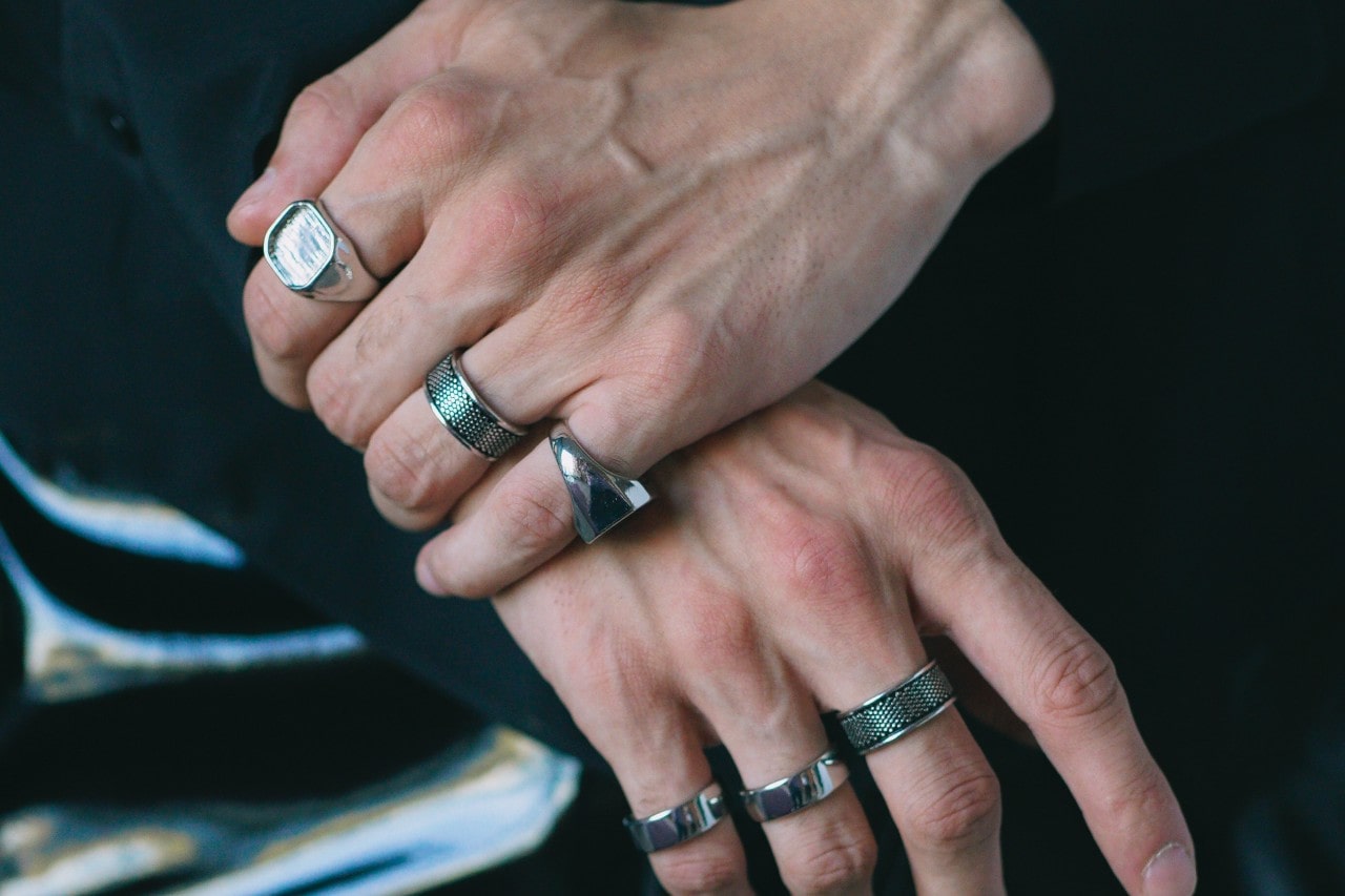 a man’s hands crossed over one another, adorned with chunky silver fashion rings