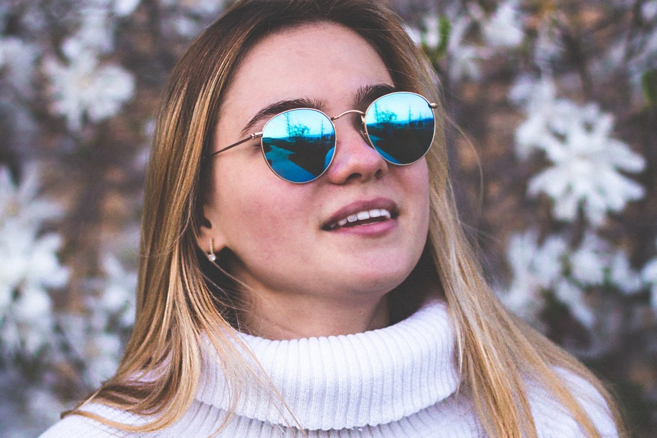 a woman in a white sweater and sunglasses wearing a pair of diamond drop earrings
