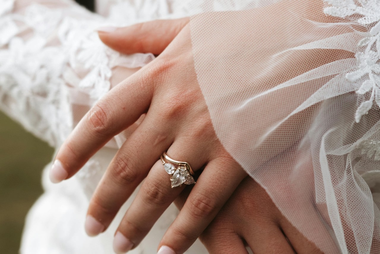 close up image of a brides hand wearing a three stone engagement ring and curved wedding band