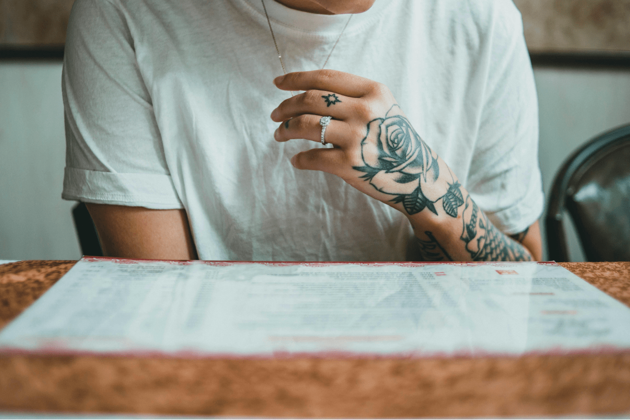 a woman with tattoos sitting at a restaurant and wearing a diamond engagement ring