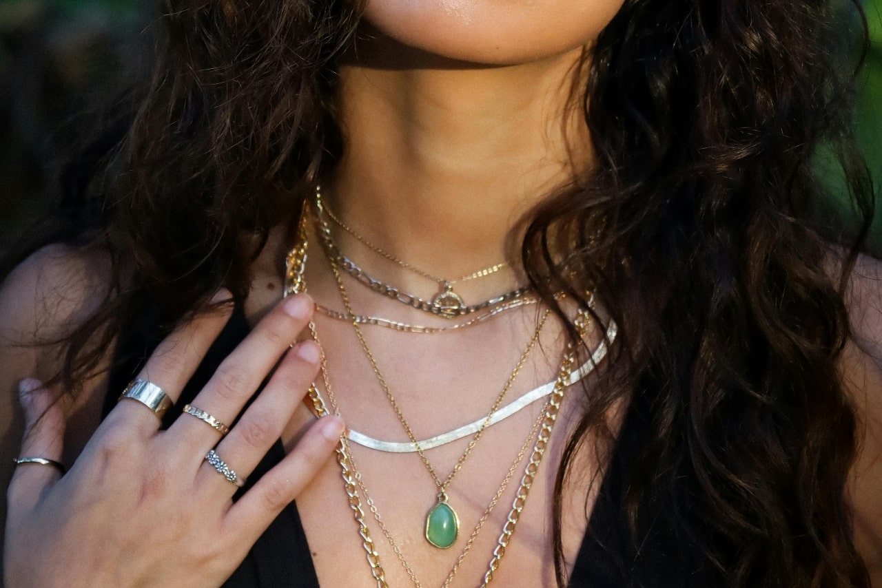 A close up of a woman with layered gold necklaces of different length and metal color.