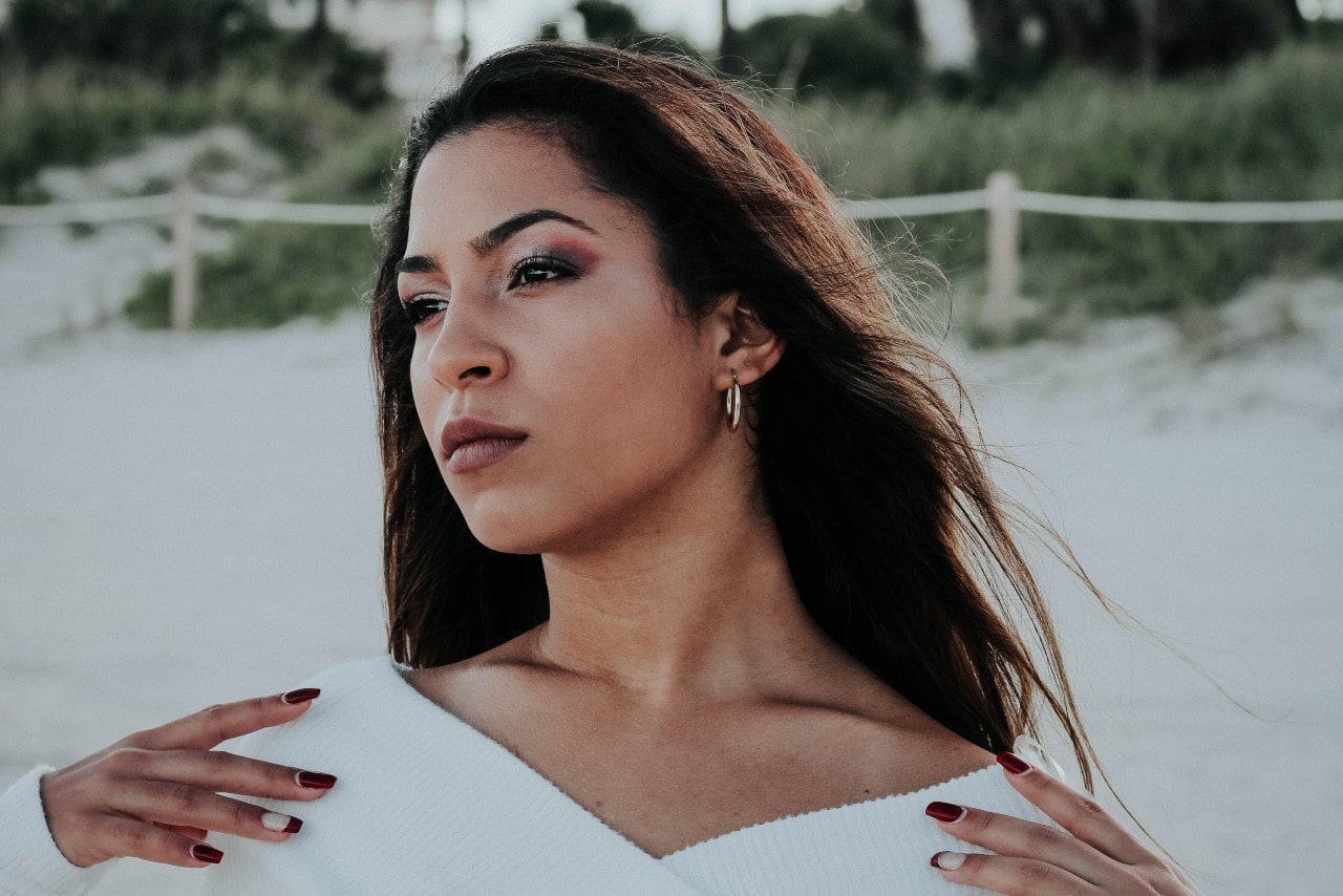 a woman standing on a beach, looking past the camera and wearing a pair of small hoop earrings