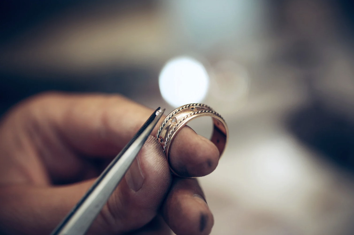 A jeweler working on a detailed gold wedding band with his tools.