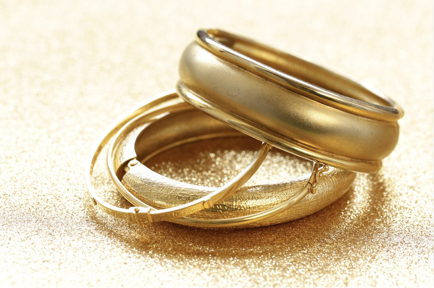 Different yellow gold rings stacked on top of each other on top of a gold sparkly surface.