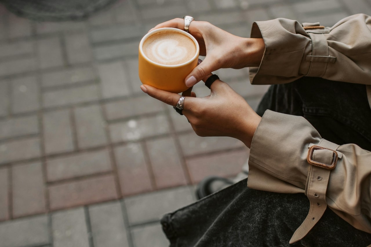A close up of hands holding a cup of coffee, adorned with bold fashion rings.