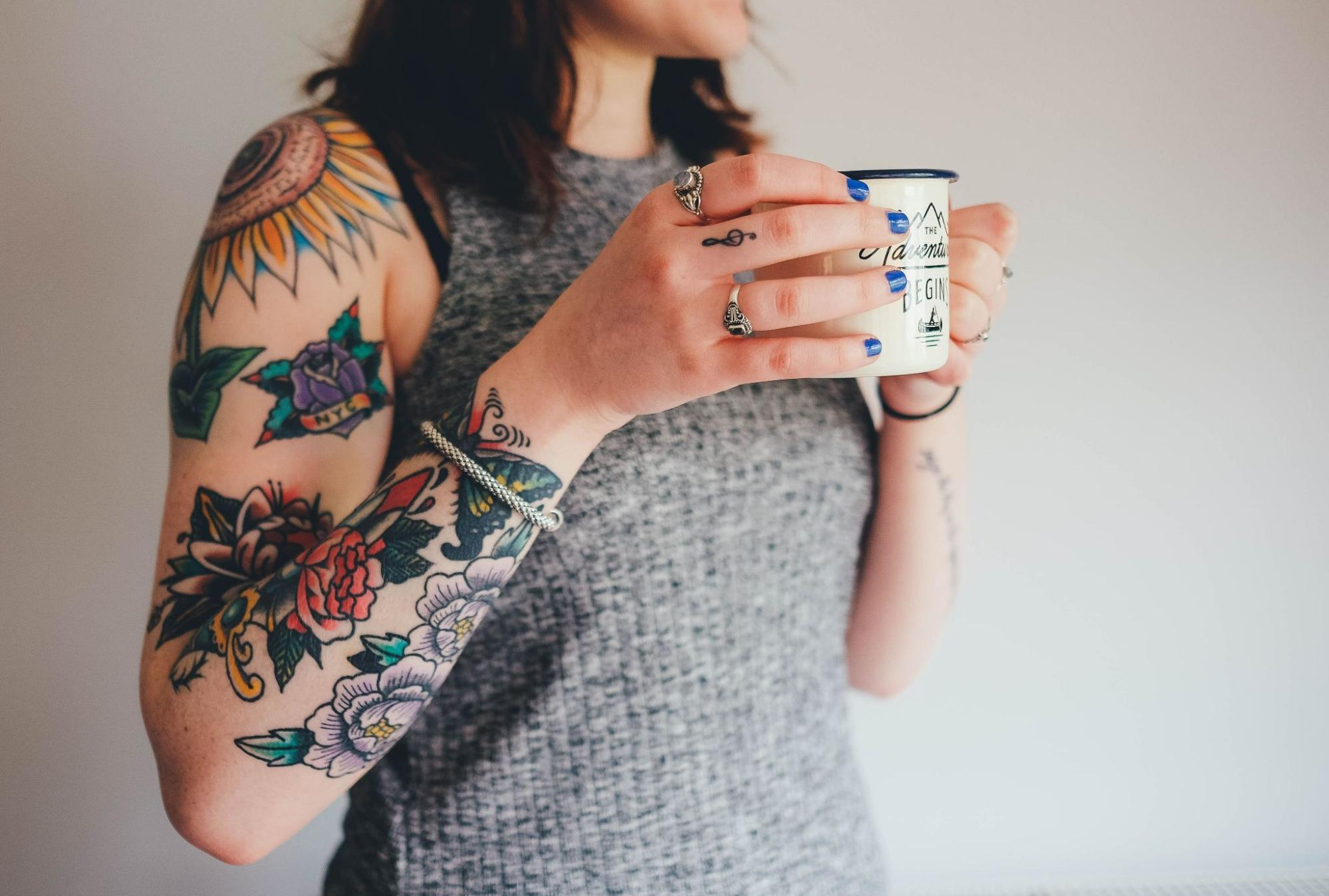 A woman with tattoos holds a mug while wearing a white gold cable-style bangle.