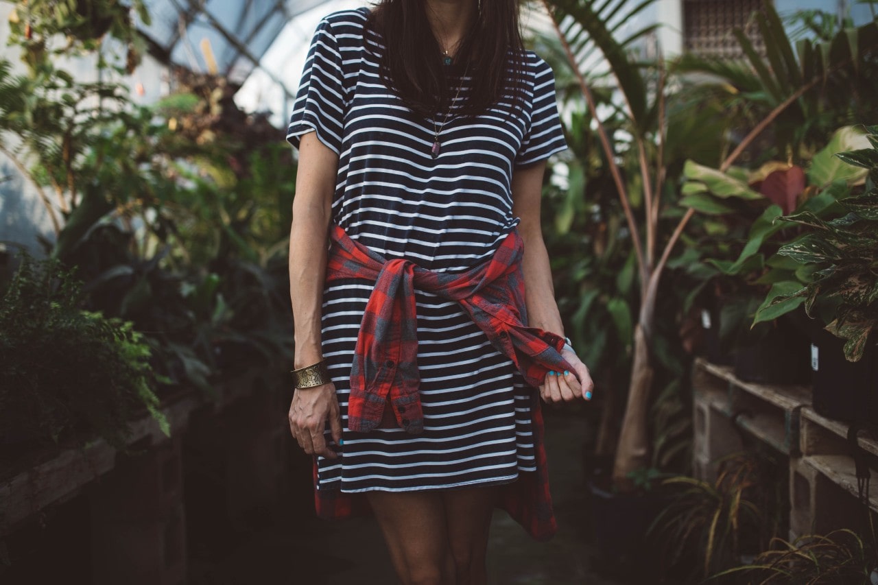 A woman in a greenhouse wearing a striped t-shirt dress and a hammered gold bangle.