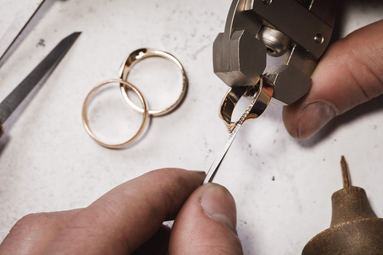 A close-up of a jeweler creating a custom wedding band, with two additional bands visible beside his hand.