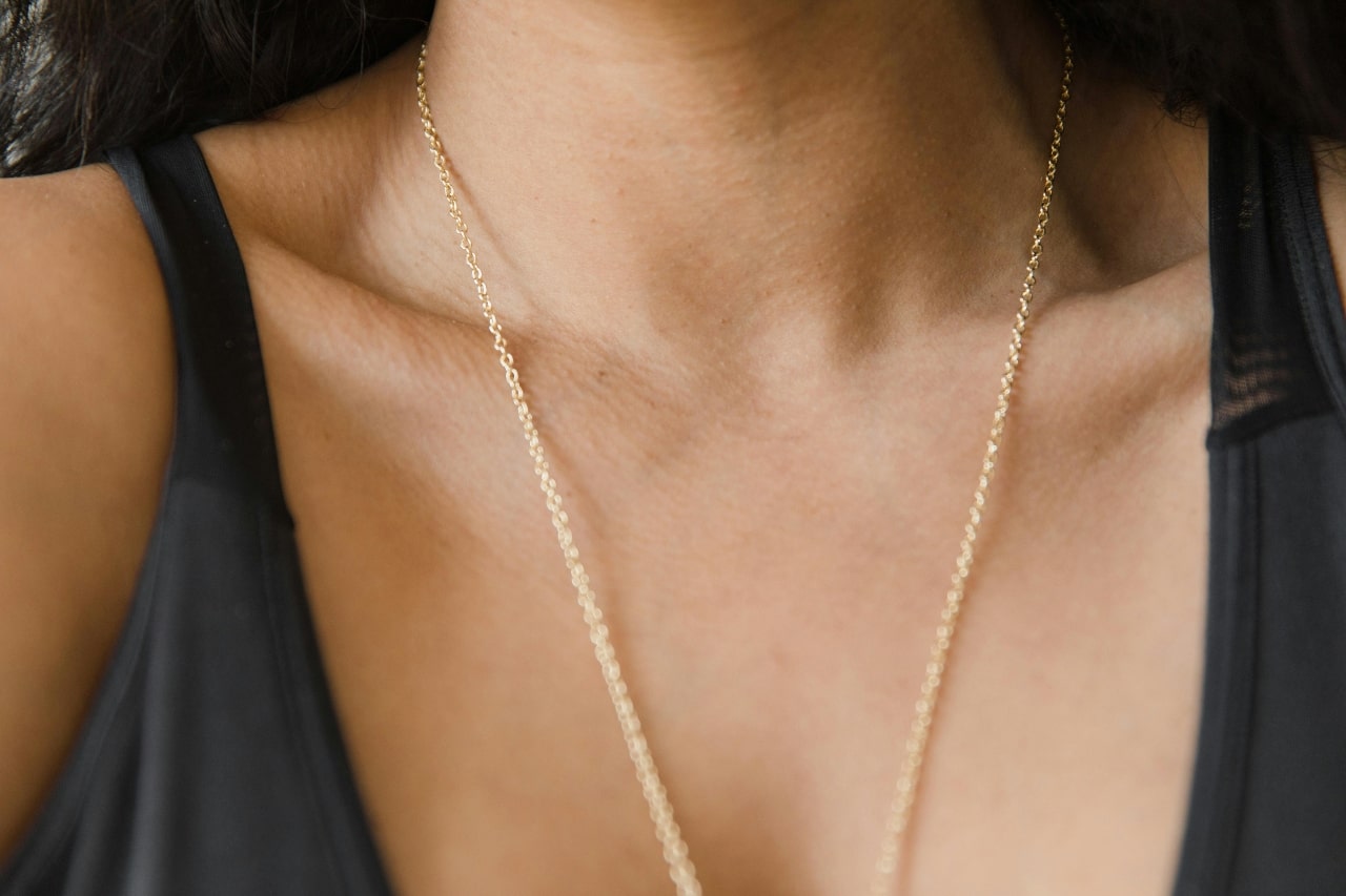 A woman a dainty long yellow gold chain with a pendant out of view. A woman a dainty long yellow gold chain with a pendant out of view.