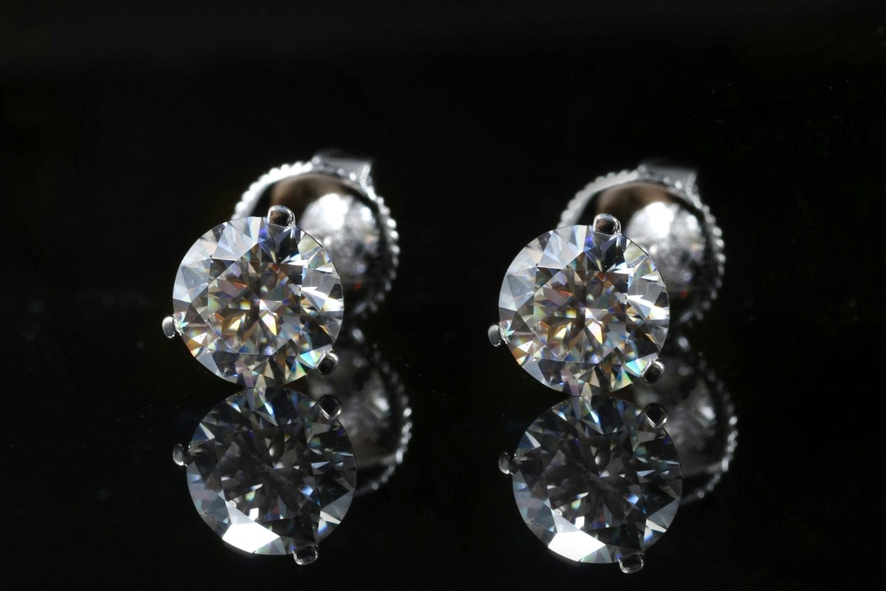 A close-up of a pair of diamond stud earrings on a black surface.