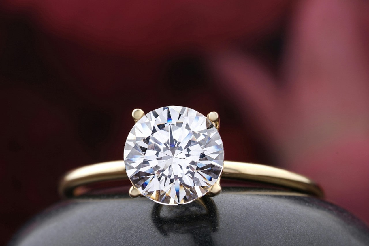 A close-up image of a round cut diamond solitaire engagement ring with gold setting.