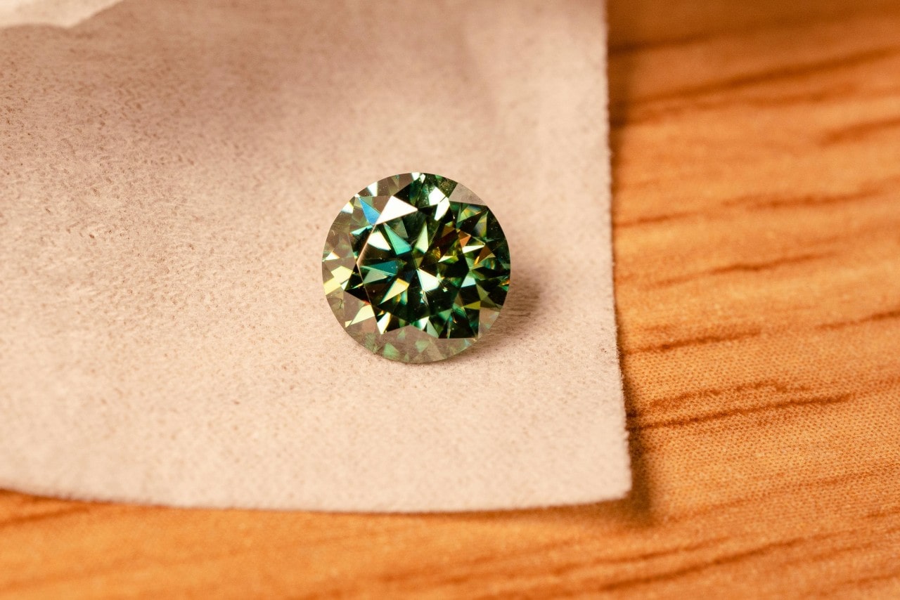 a green round cut diamond ona piece of beige fabric