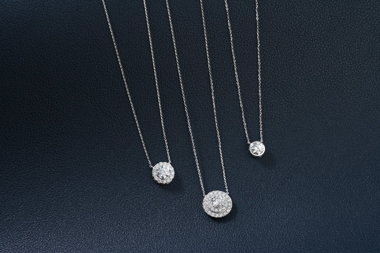 three diamond necklaces wrought in silver toned metal on a black surface