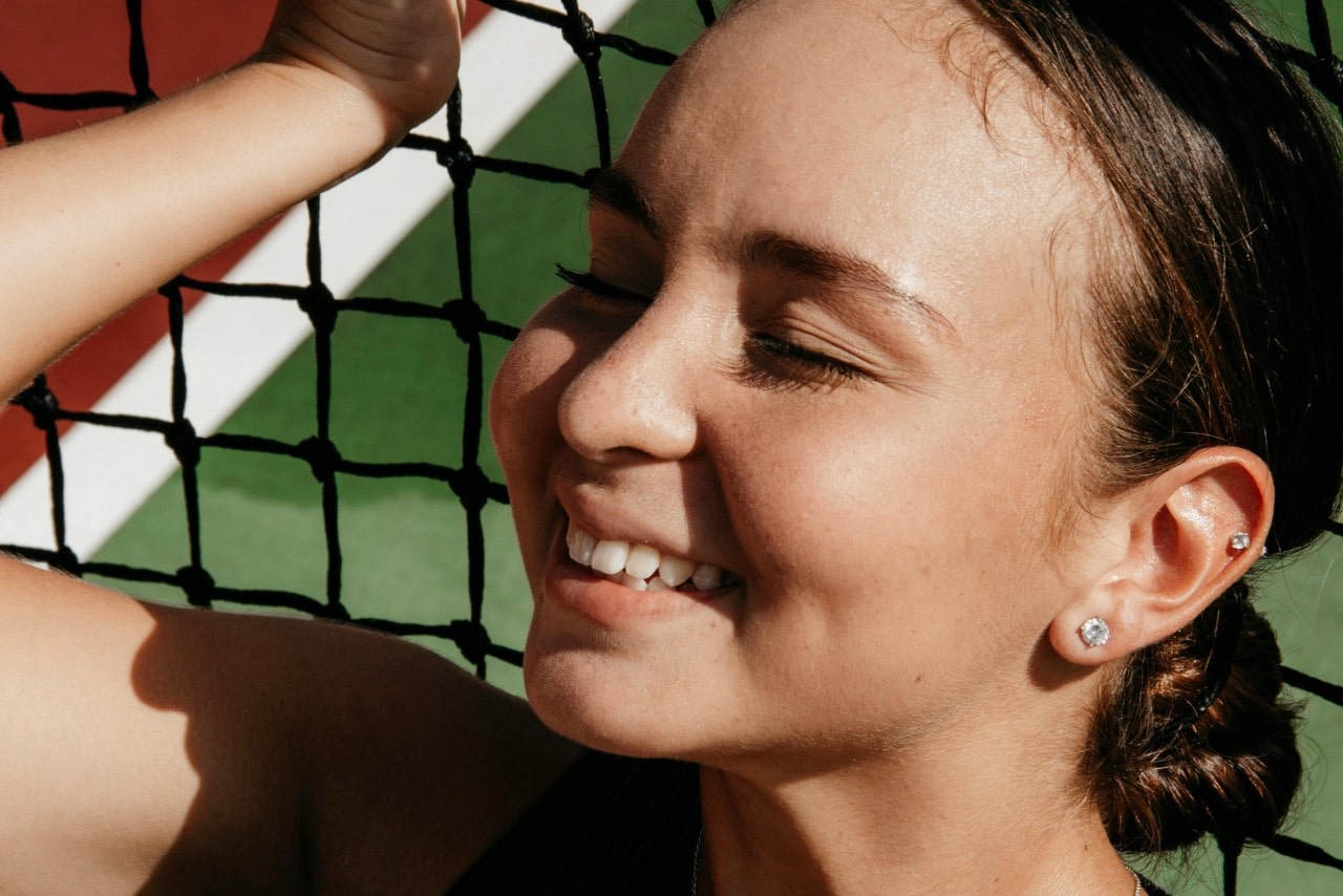 A close-up of a happy young woman wearing stud earrings as she relaxes against a net. A close-up of a happy young woman wearing stud earrings as she relaxes against a net.