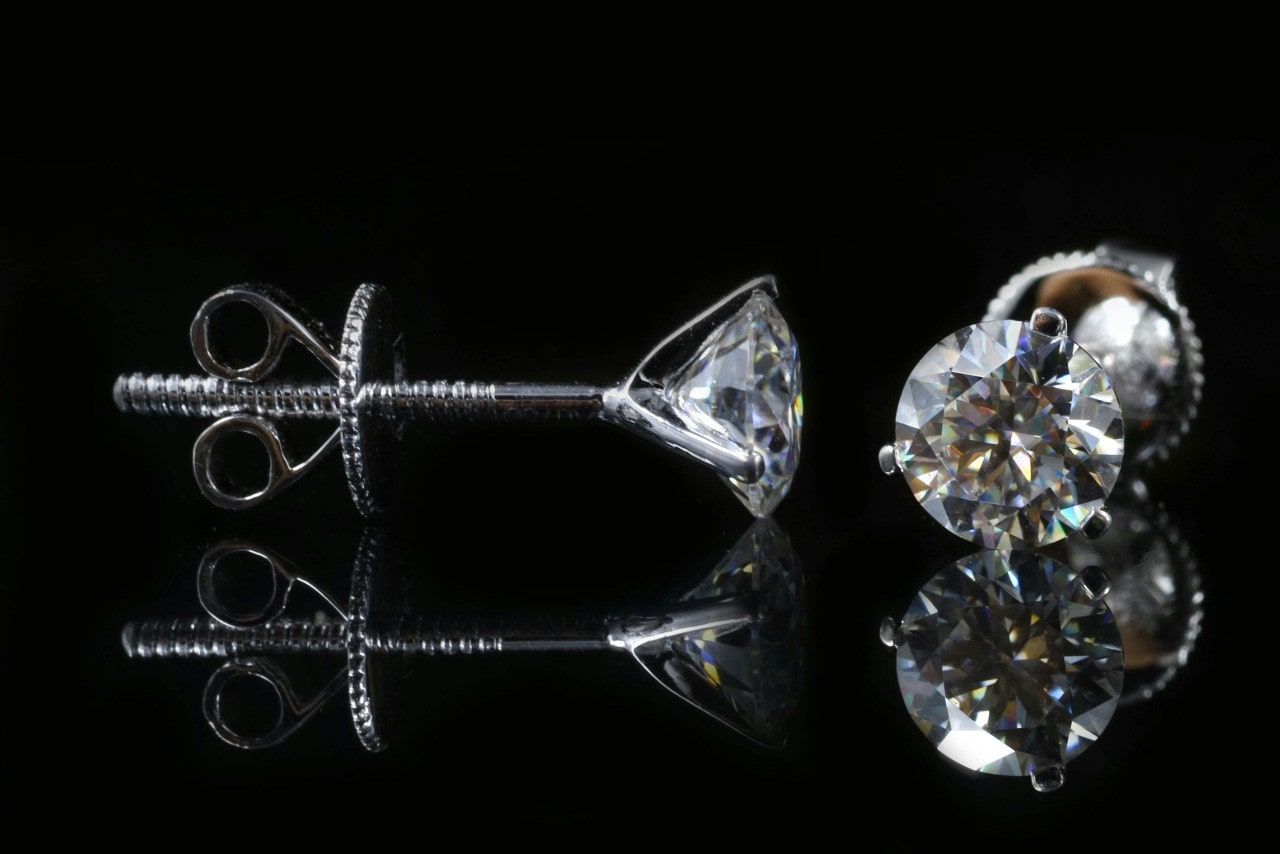 A close-up of elegant diamond studs on a black background. A close-up of elegant diamond studs on a black background.