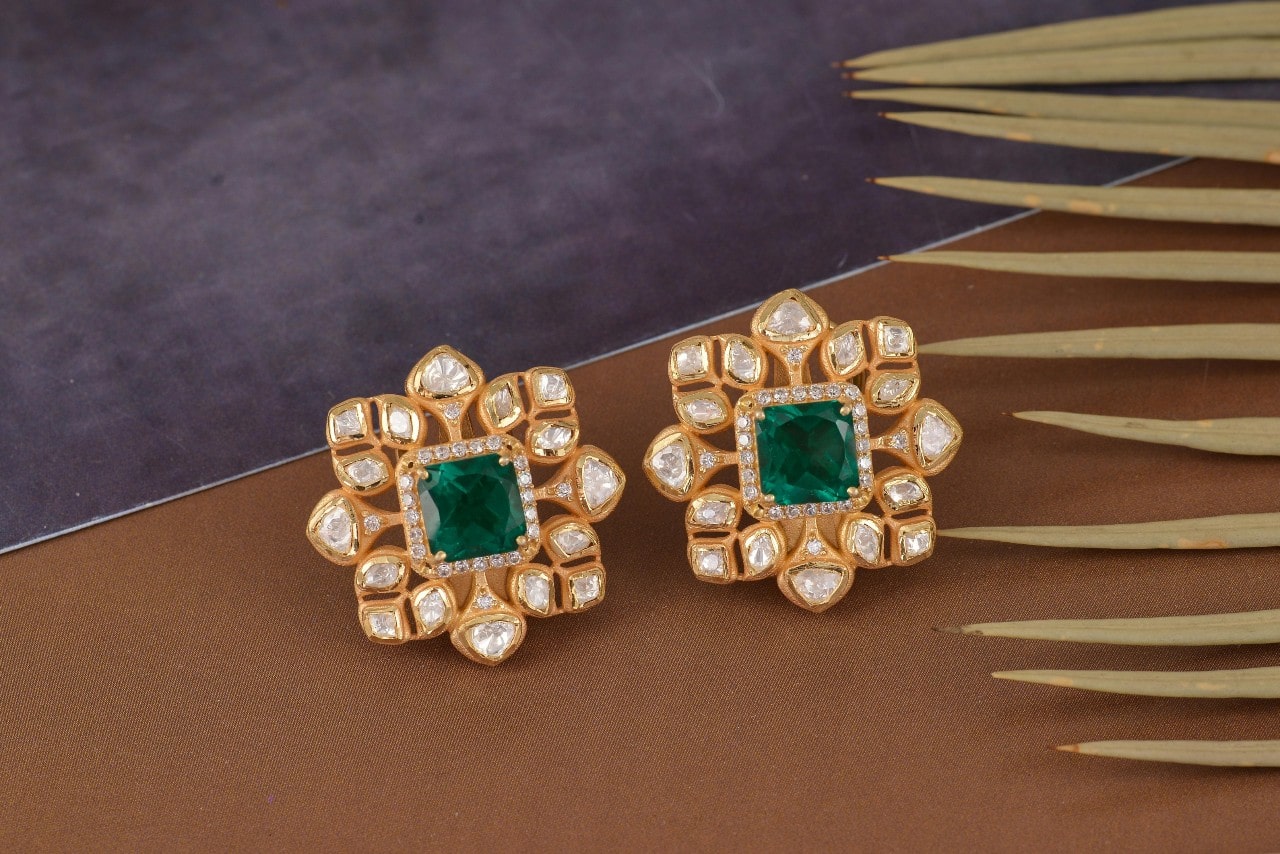 A close-up of elegant and distinctive diamond and emerald stud earrings. A close-up of elegant and distinctive diamond and emerald stud earrings.