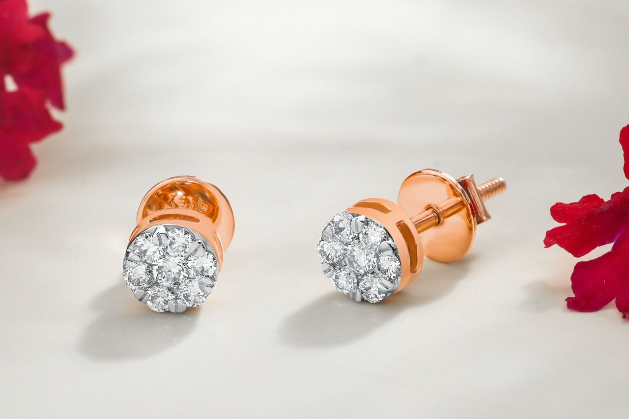 a pair of rose gold diamond stud earrings sit by red flower petals on a white fabric. a pair of rose gold diamond stud earrings sit by red flower petals on a white fabric.