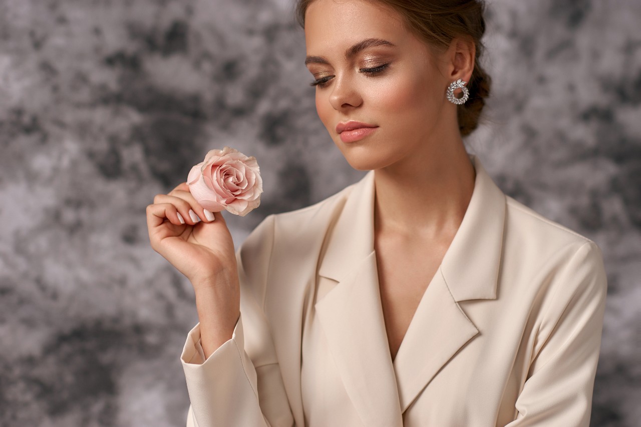 a business woman holds a flower while wearing circle diamond earrings. a business woman holds a flower while wearing circle diamond earrings.
