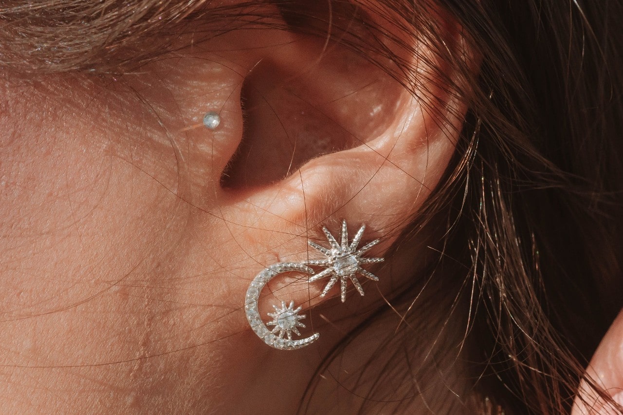 A woman’s ear with multiple piercings wearing celestial diamond earrings. A woman’s ear with multiple piercings wearing celestial diamond earrings.
