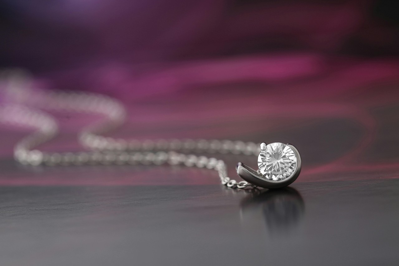 a white gold diamond pendant necklace on a purple and black surface a white gold diamond pendant necklace on a purple and black surface