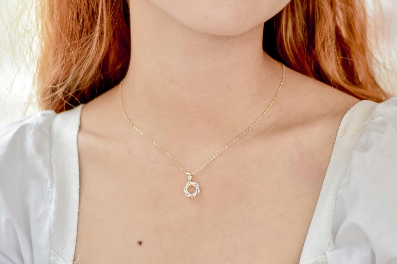 close up image of a woman’s neckline adorned with a yellow gold diamond pendant close up image of a woman’s neckline adorned with a yellow gold diamond pendant
