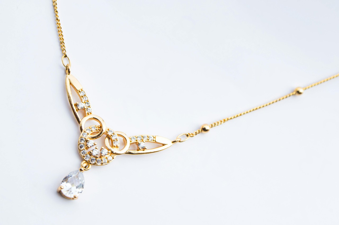 close up image of a yellow gold necklace with a pear shape diamond and intricate details close up image of a yellow gold necklace with a pear shape diamond and intricate details