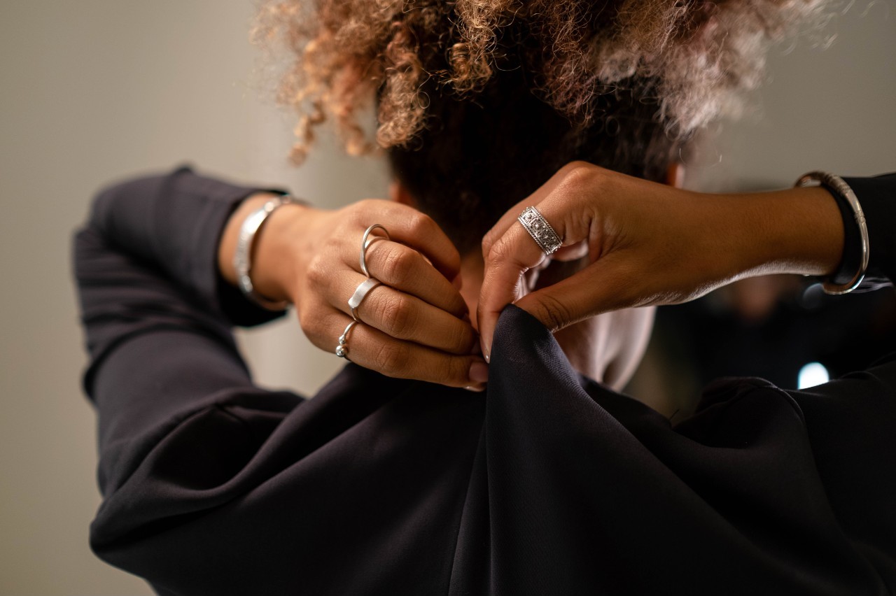 A woman puts on a black longsleeve, showcasing stackable silver fashion rings. A woman puts on a black longsleeve, showcasing stackable silver fashion rings.