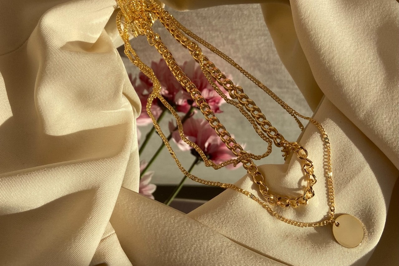 Several yellow gold necklaces on a mirror, surrounded by yellow fabric. Several yellow gold necklaces on a mirror, surrounded by yellow fabric.