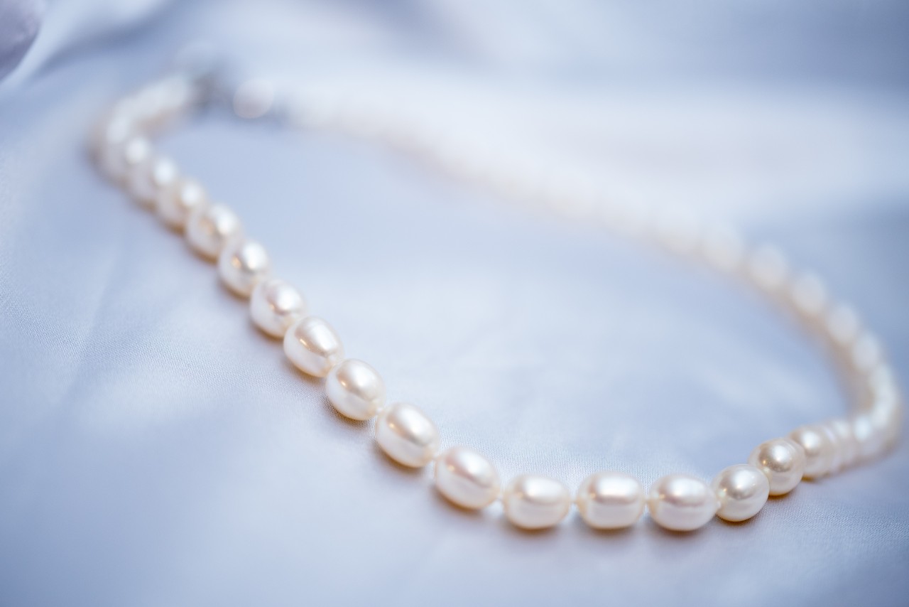 A delicate pearl necklace rests on a smooth, light blue satin fabric.