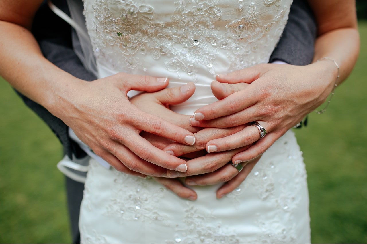 a man’s arms wrapped around a woman’s torso, both wearing wedding bands