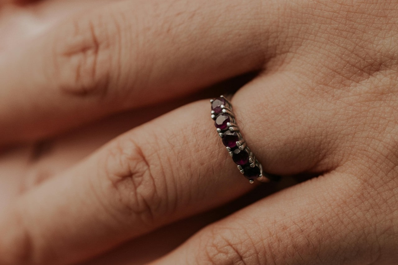 A close up of a person’s finger, adorned in a wedding band with prong set, round cut rubies.