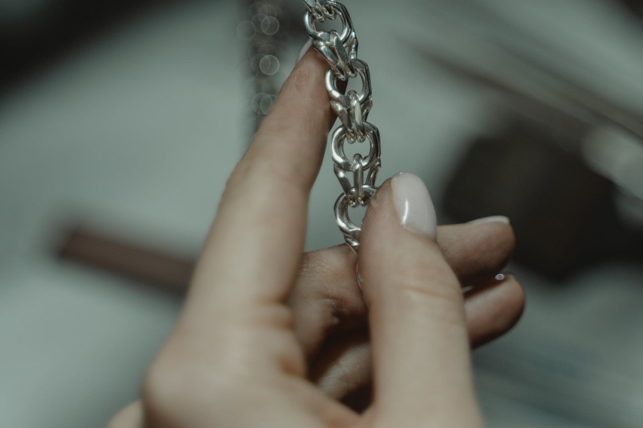 A close-up of a woman’s hand holding a chain bracelet and inspecting the links. A close-up of a woman’s hand holding a chain bracelet and inspecting the links.