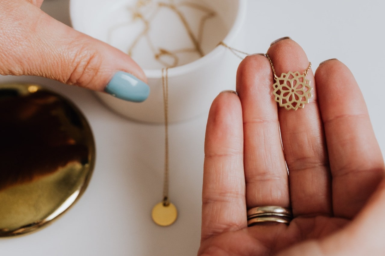 A close-up of a woman’s hands selecting a necklace from a small jewelry box, and holding it in her palm. A close-up of a woman’s hands selecting a necklace from a small jewelry box, and holding it in her palm.