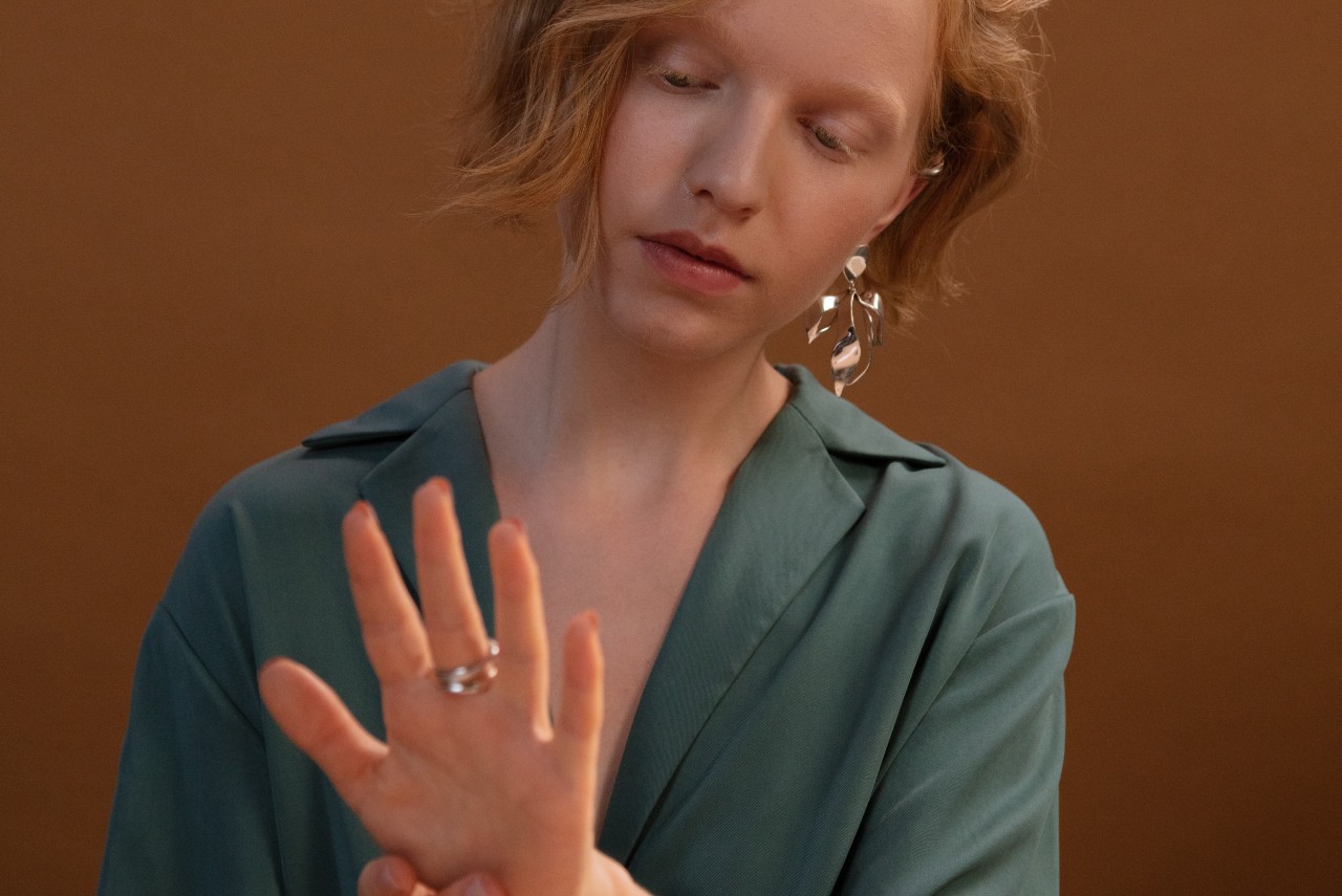 A photo of a young woman wearing an ornate earring, glancing down to the ring stack on her finger. A photo of a young woman wearing an ornate earring, glancing down to the ring stack on her finger.