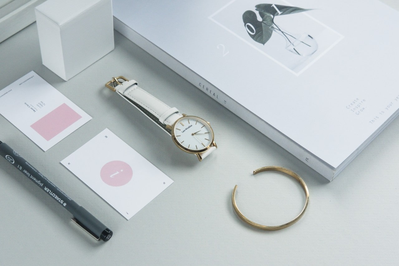 A close up of several items on white surface, including an open bangle, a wristwatch with white dial and strap,a grey pen and two small cards. A close up of several items on white surface, including an open bangle, a wristwatch with white dial and strap,a grey pen and two small cards.