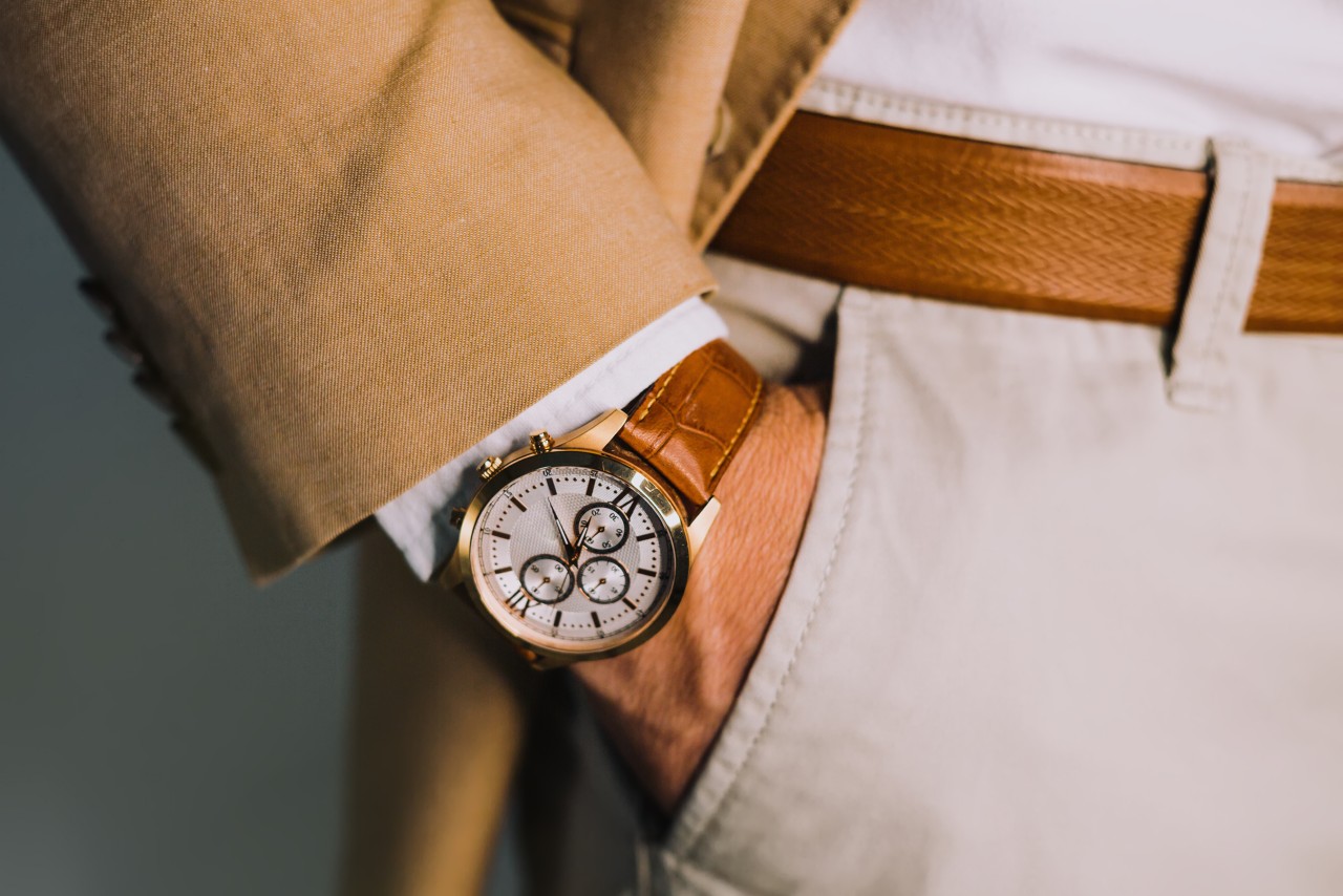 A close up of man’s hand in the pocket of his white trousers, showcasing a brown leather watch that matches his belt. A close up of man’s hand in the pocket of his white trousers, showcasing a brown leather watch that matches his belt.