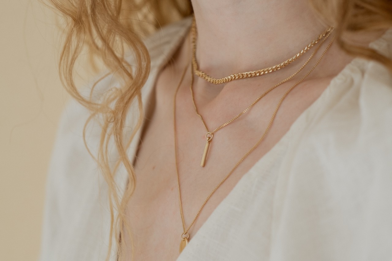 close up image of a woman’s neck, adorned with three gold necklaces of varying lengths