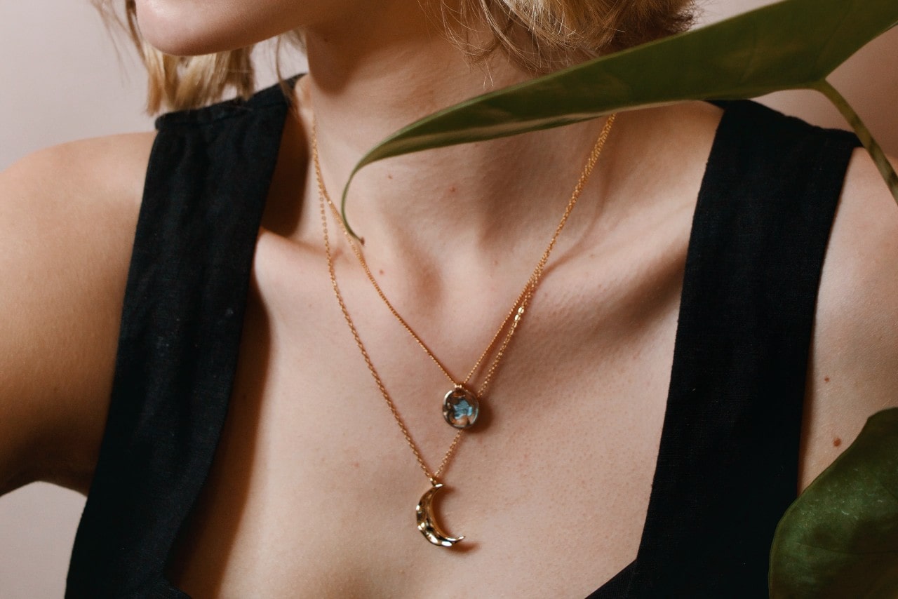 close up image of a woman’s chest, adorned with two yellow gold pendant necklaces