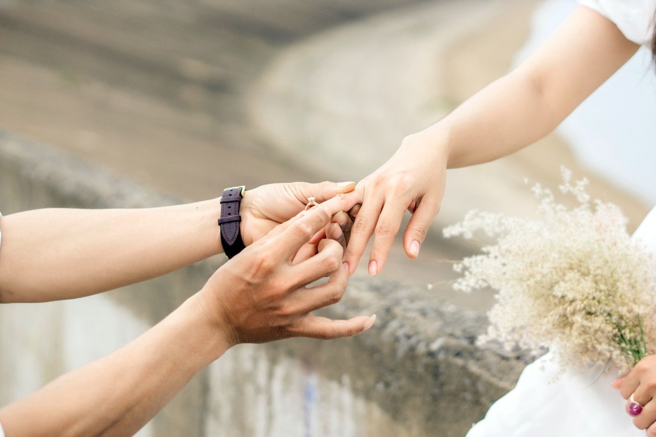 A person slips an engagement ring onto a bride’s ring finger.