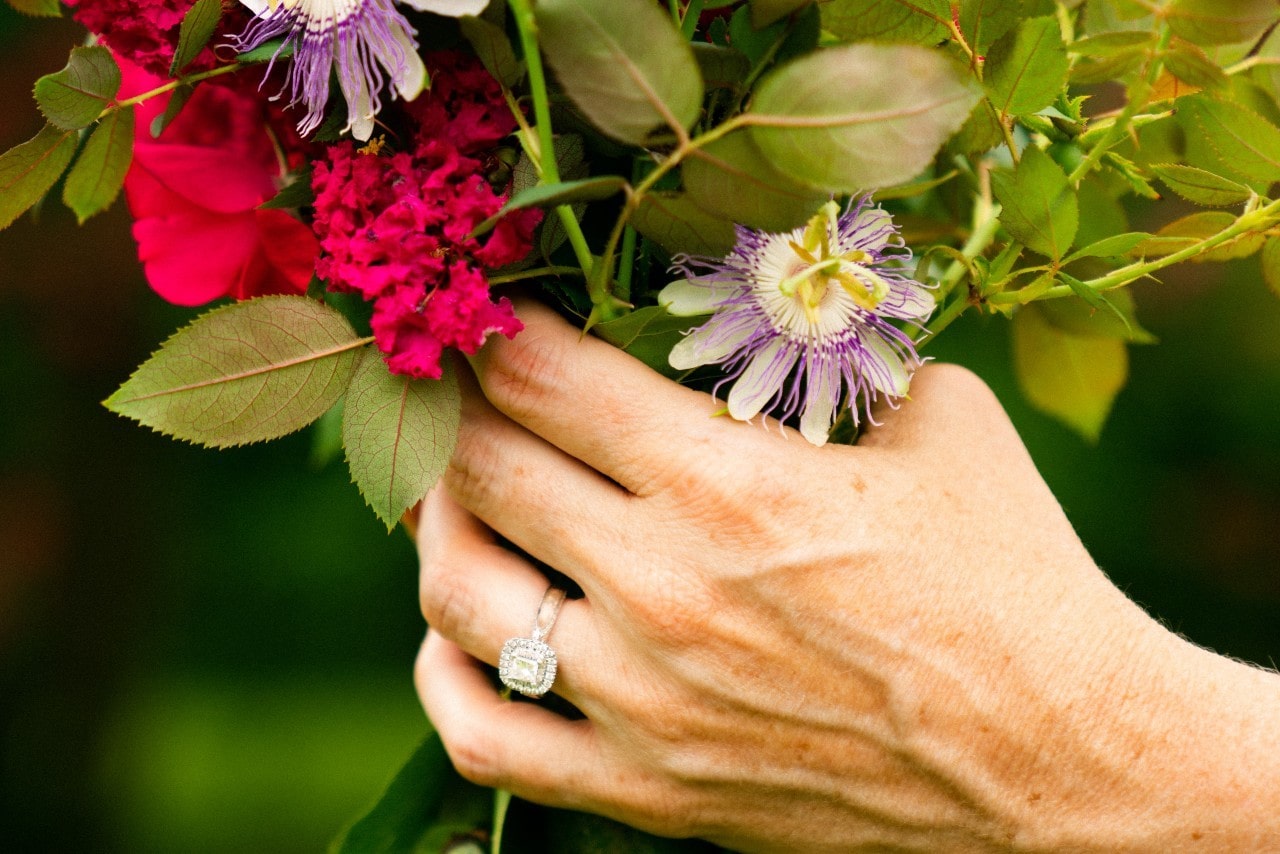 A woman’s hand wearing a halo radiant-cut diamond ring holding flowers.