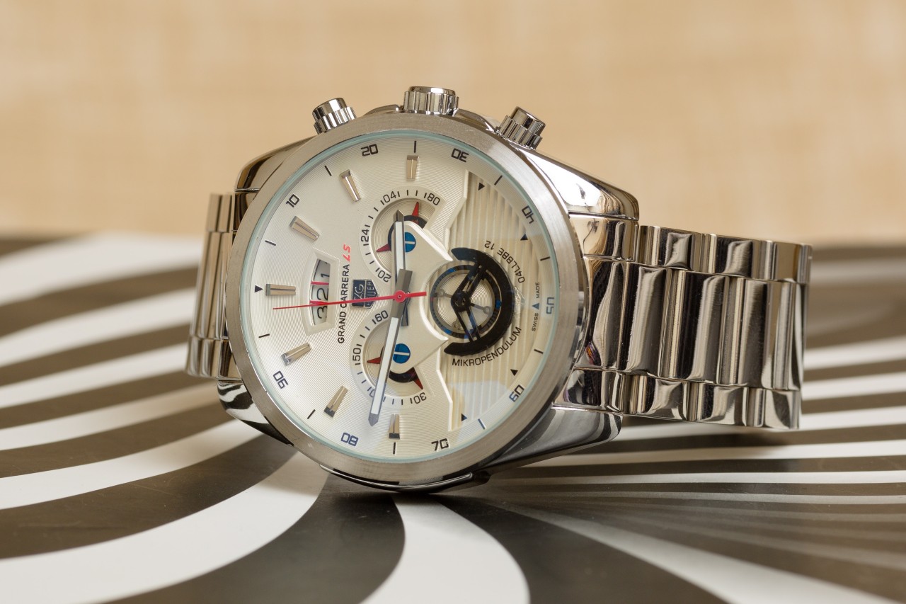 A silver Tag Heuer watch with a white dial and three subdials on a black and white surface A silver Tag Heuer watch with a white dial and three subdials on a black and white surface