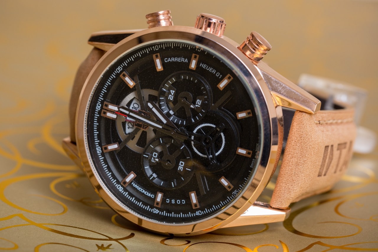 Close up image of a gold and black TAG Heuer watch on a tan and gold surface Close up image of a gold and black TAG Heuer watch on a tan and gold surface