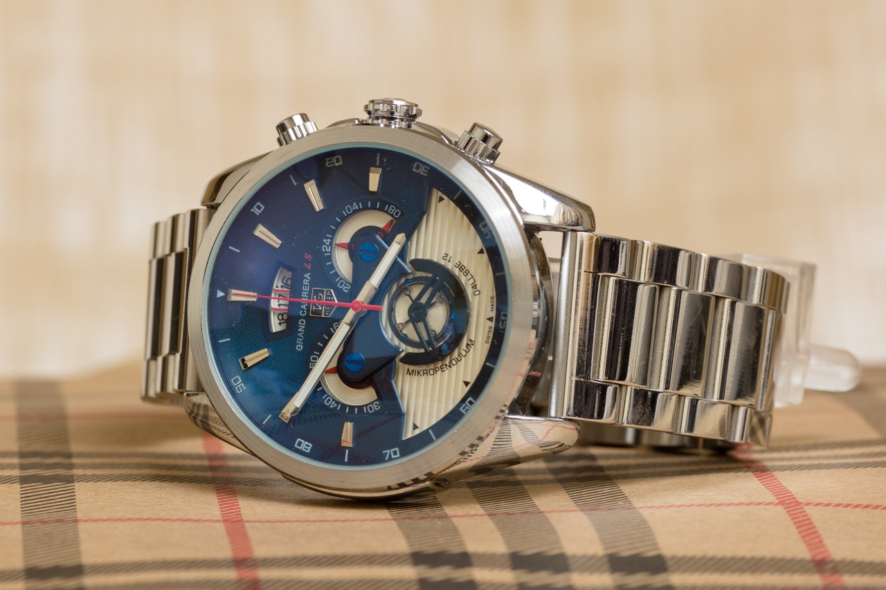 A silver TAG Heuer watch with a blue watch face on a plaid surface