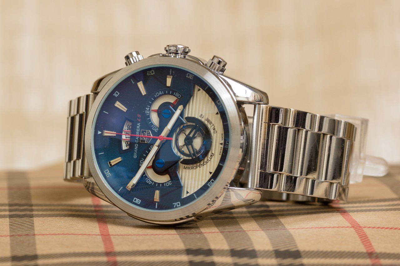 A silver TAG Heuer watch with a blue watch face on a plaid surface A silver TAG Heuer watch with a blue watch face on a plaid surface