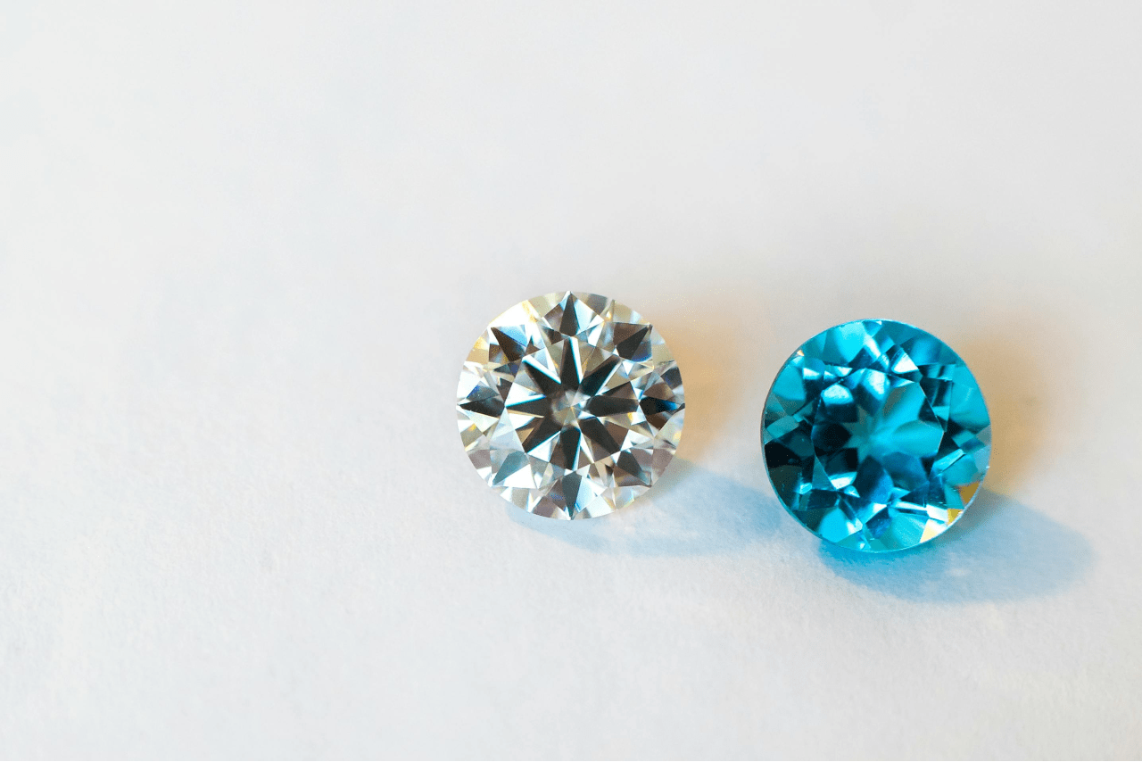 A colorless round cut diamond next to a blue one on a pale backdrop.