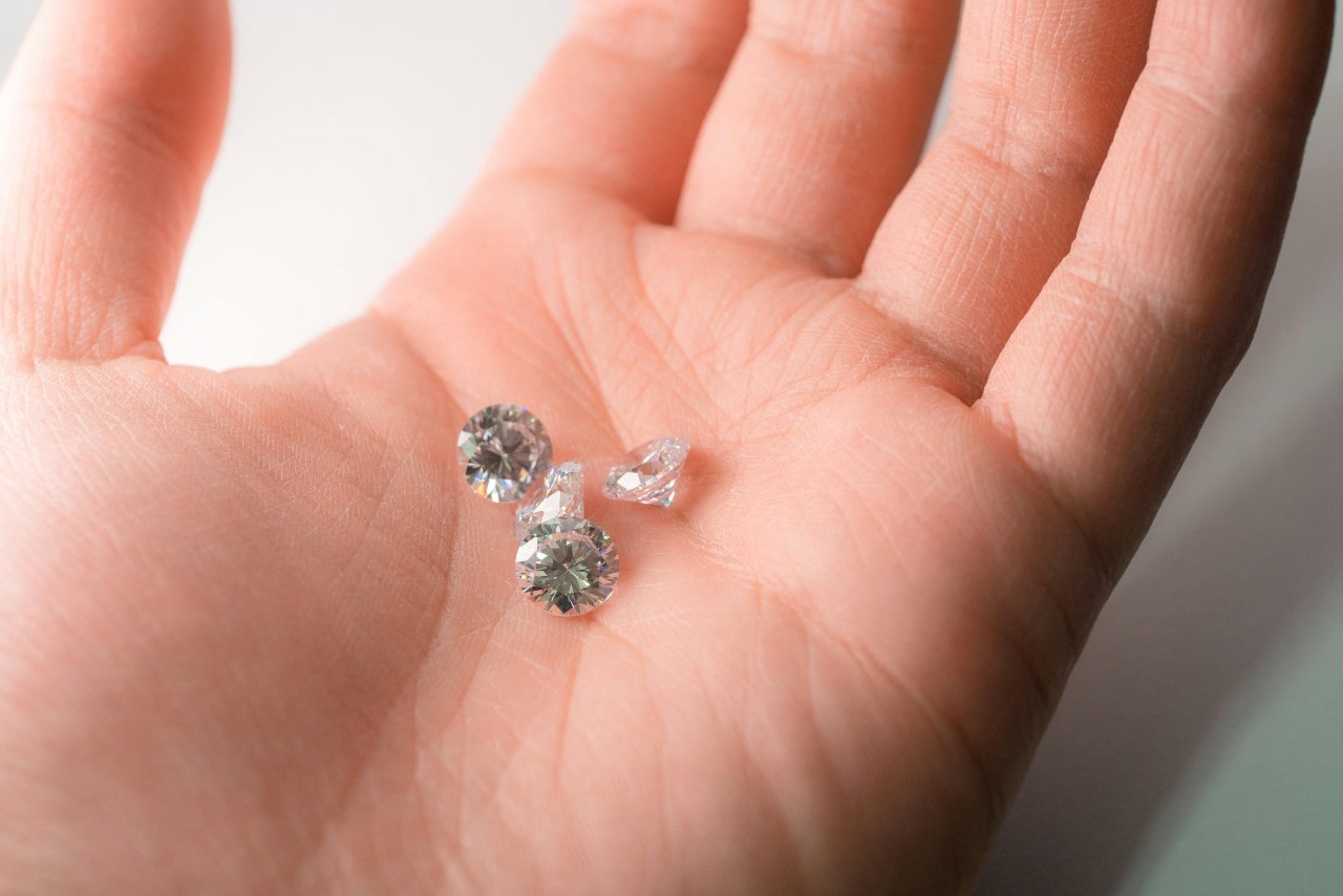 A close-up of four round cut diamonds sitting in the palm of a person’s hand.