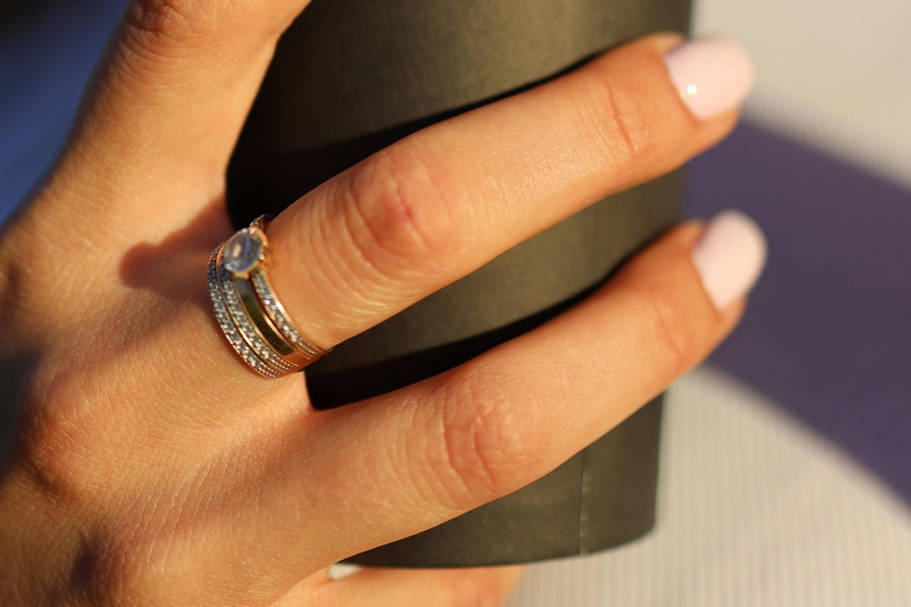 A woman holding a paper coffee cup, showcasing her side stone engagement ring and wedding band.