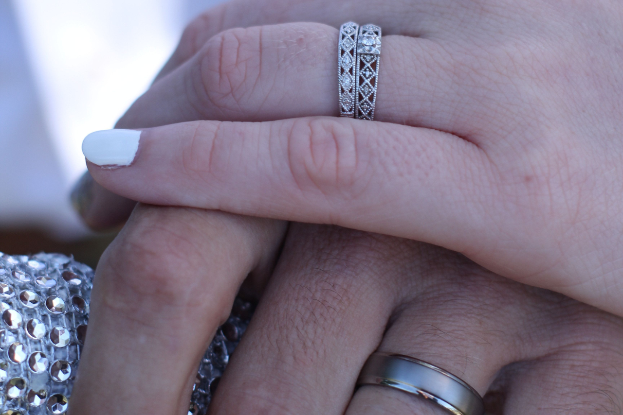 A woman laying her hand on a man’s hand, showcasing their gorgeous wedding bands.