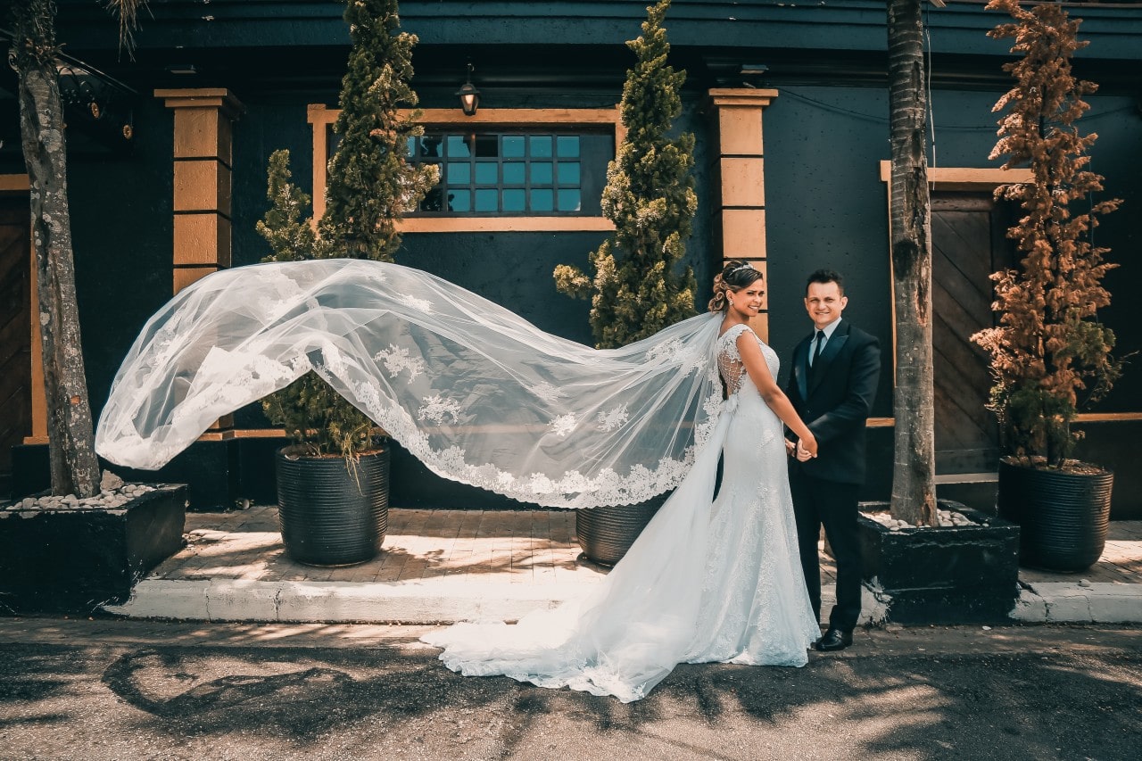 A bride and groom posing in front of a dark building, the bride’s long veil blowing in the wind. A bride and groom posing in front of a dark building, the bride’s long veil blowing in the wind.